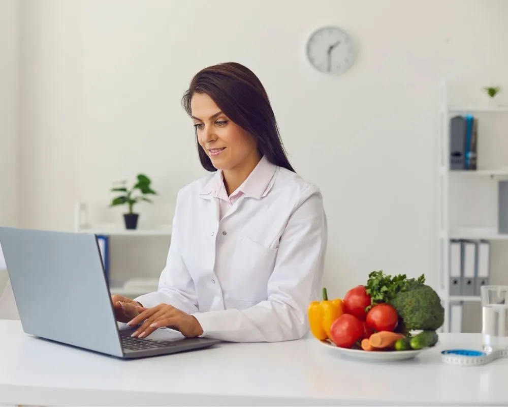 A health coach reviewing a plan at a desk with fresh vegetables nearby.